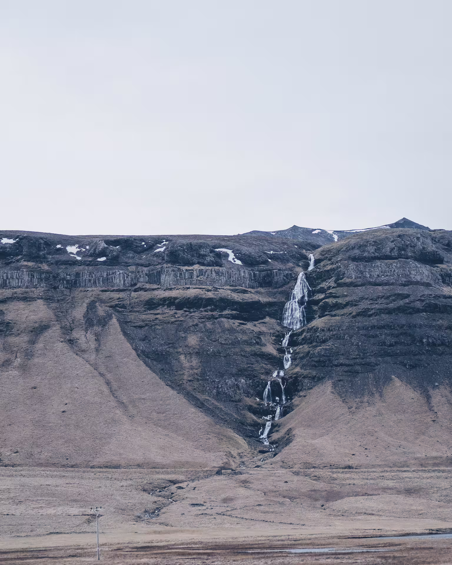 Cascading waterfall down volcanic cliffs on Snaefellsnes Peninsula with snow-dusted ridgeline