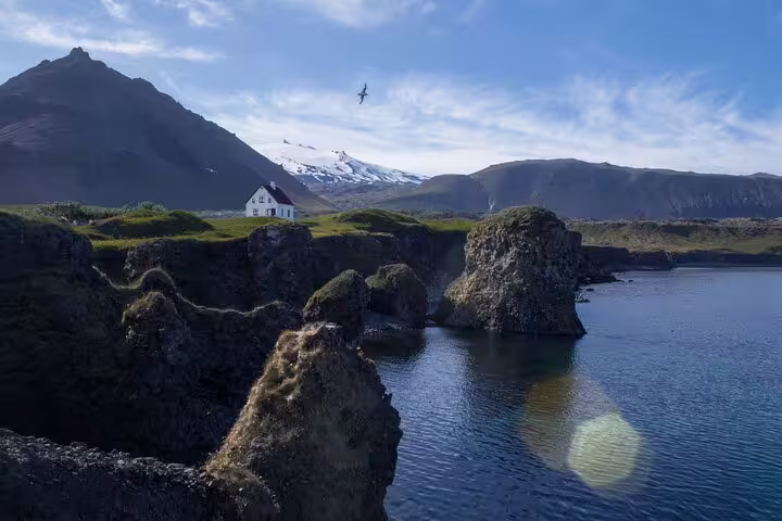 Rocky coastal cliffs with a white house and snow-capped Snæfellsjökull volcano in Snaefellsnes, Iceland