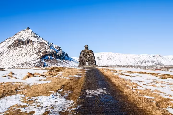 Stone monument on road leading to snow-capped Snæfellsnes mountains under clear blue sky