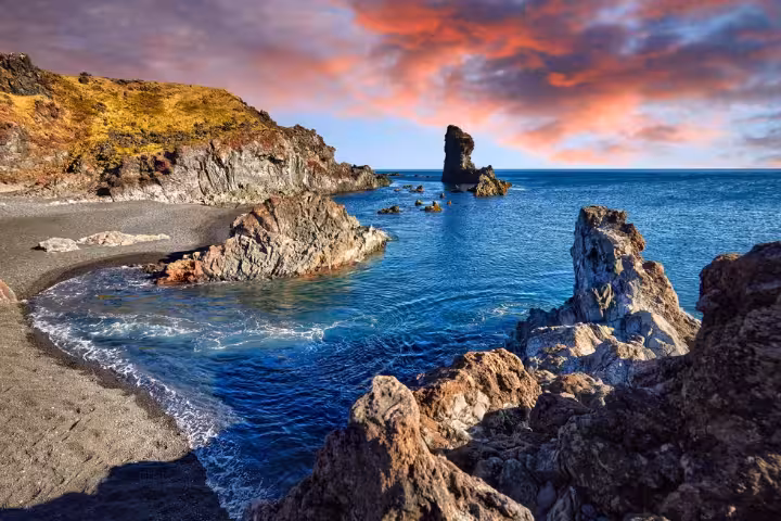 Black sand beach with volcanic rock formations and sea stack along Snaefellsnes Peninsula coastline at sunset