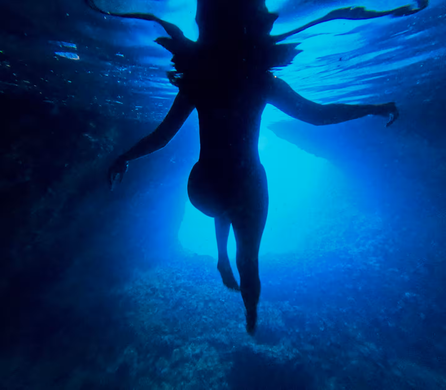 Snorkeler swimming in a hidden sea cave on the 3 Islands speedboat tour, glowing blue water and cliff walls