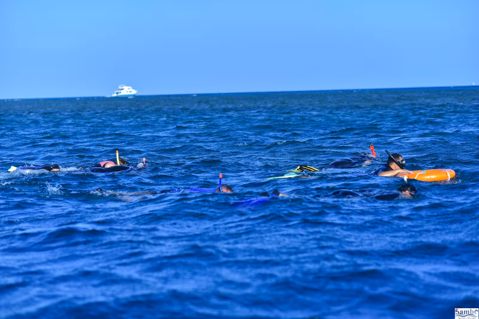 Group of snorkelers swimming at the surface of open blue sea at Sataya Reef with a yacht in the distance