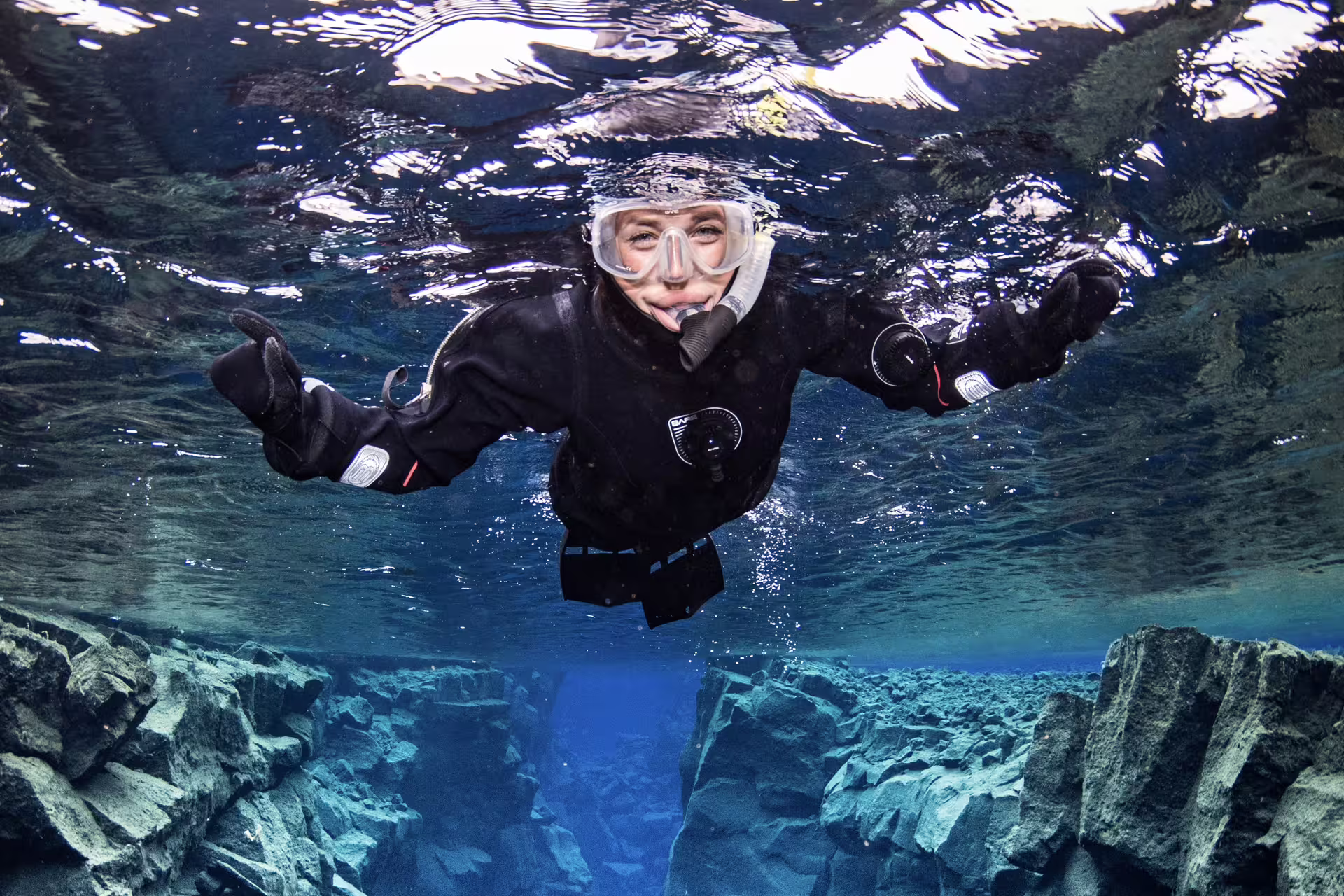 Snorkeler in black drysuit floating between rock formations in crystal clear blue water in Reykjavik