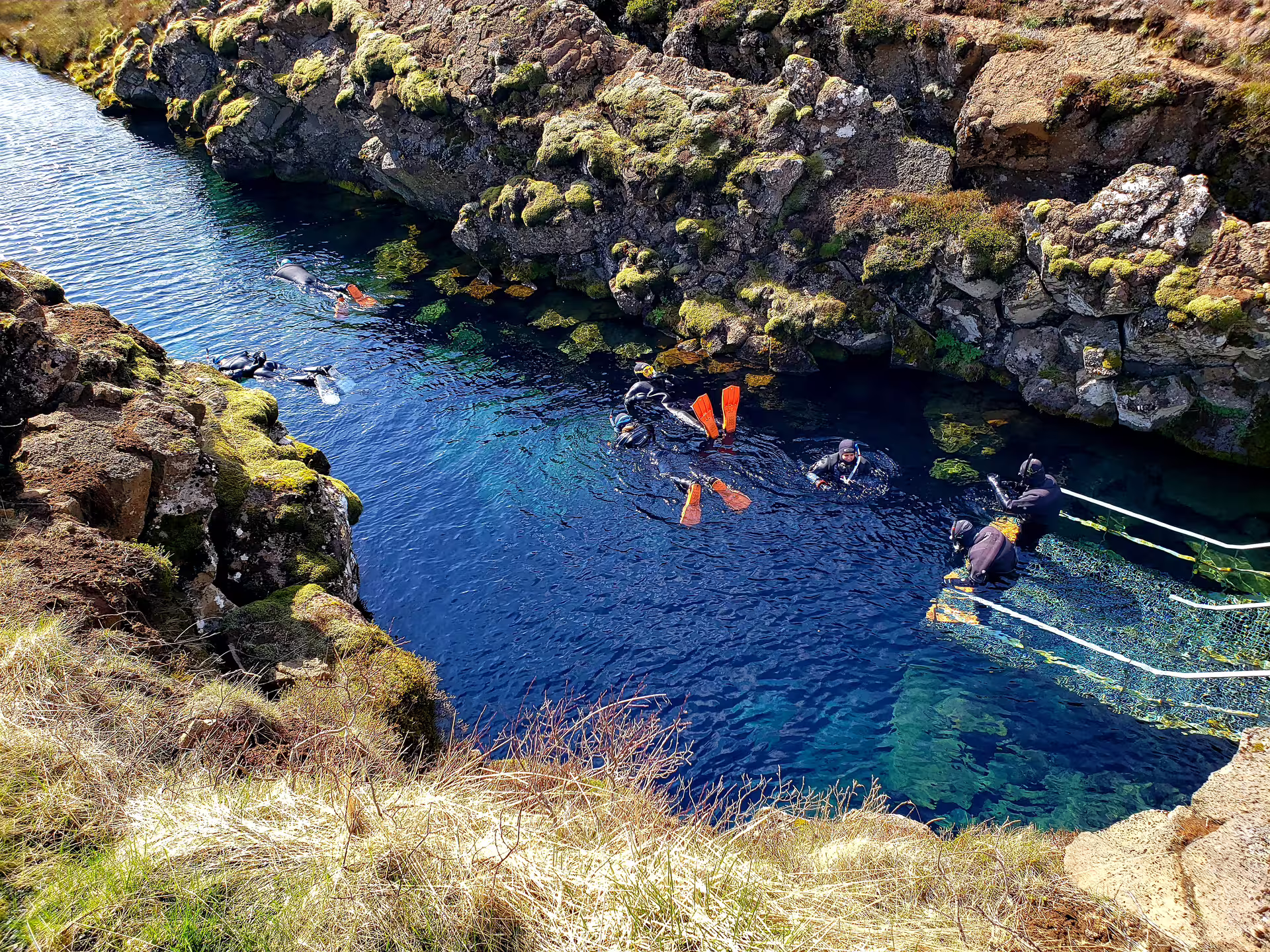Snorkelers in wetsuits floating in the crystal-clear blue waters of Silfra fissure, Iceland, surrounded by lava rocks