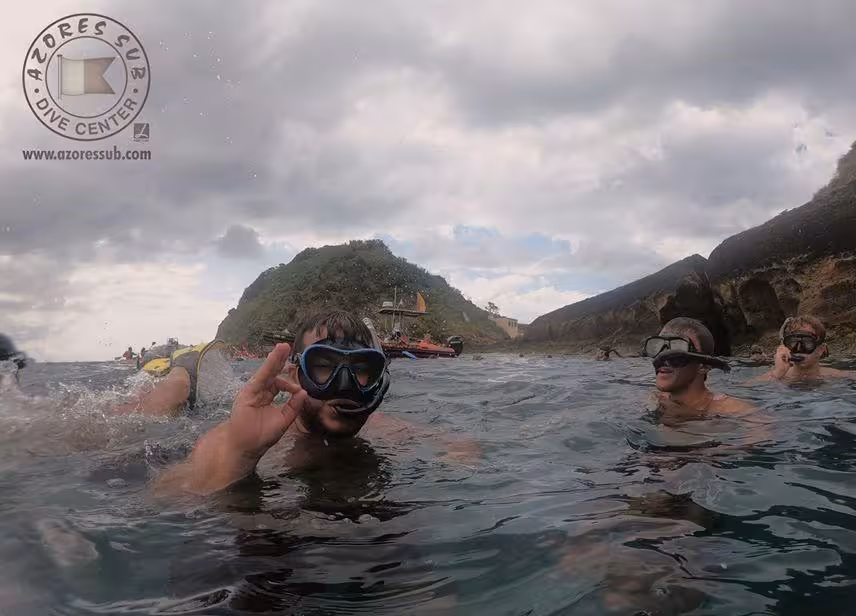 Snorkelers float near a rocky Azores coastline during a guided snorkeling excursion, giving the OK sign