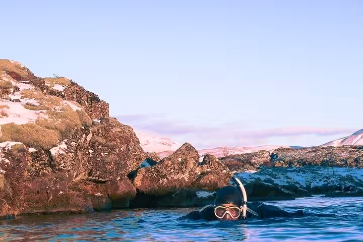 Snorkeler in wetsuit floating between volcanic rocks in icy blue waters of Iceland