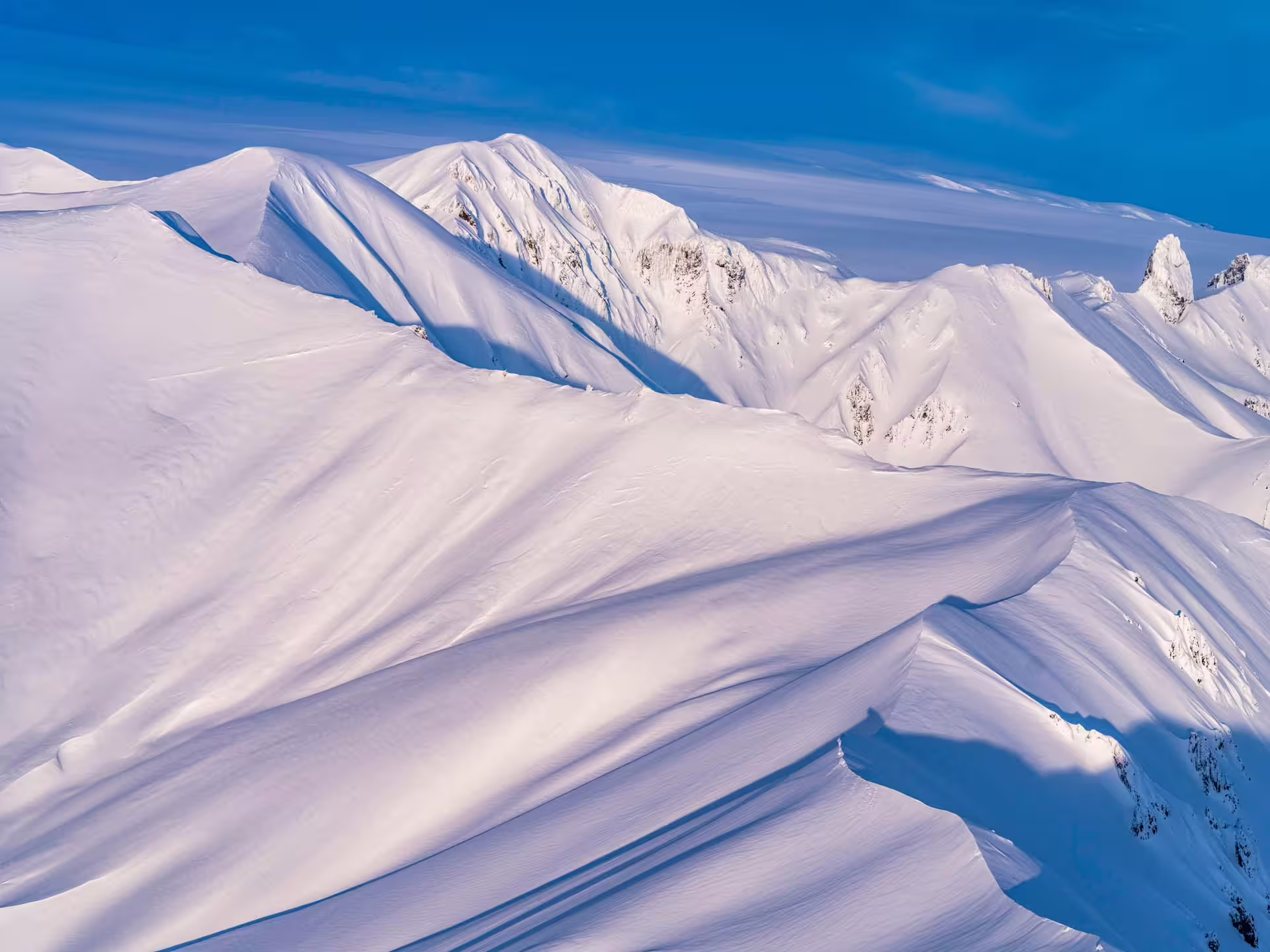 Snow-covered mountain ridges and peaks under blue sky aerial view in Iceland