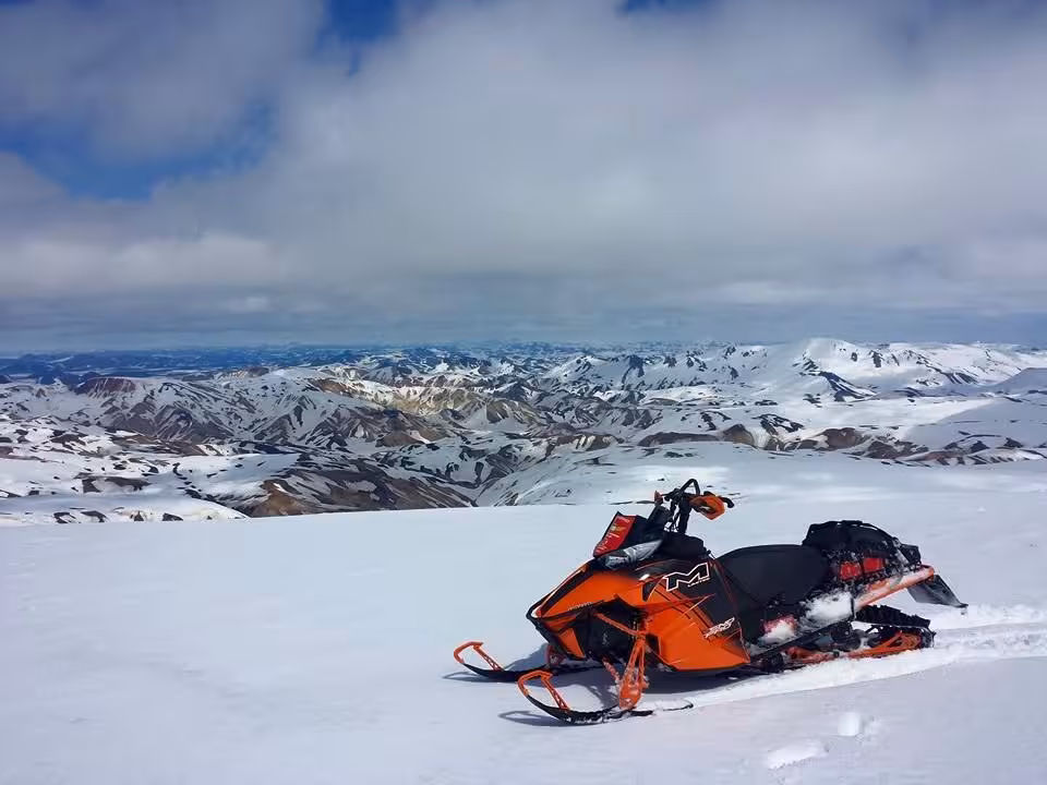 Orange Arctic Cat snowmobile parked on snowy highland plateau with panoramic mountain views in Landmannalaugar, Iceland