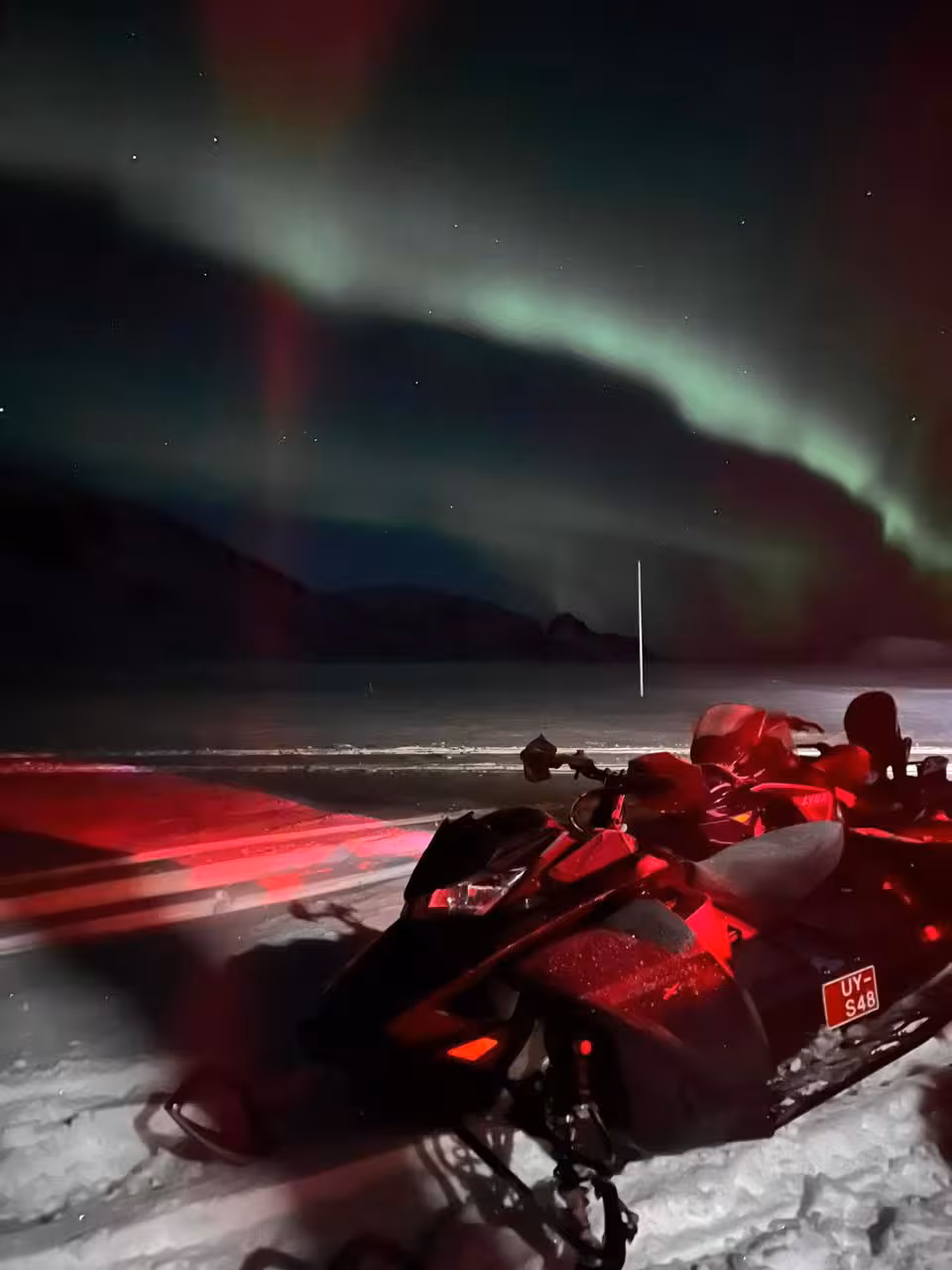 Red snowmobile parked on snow under vivid green and red northern lights aurora borealis at night
