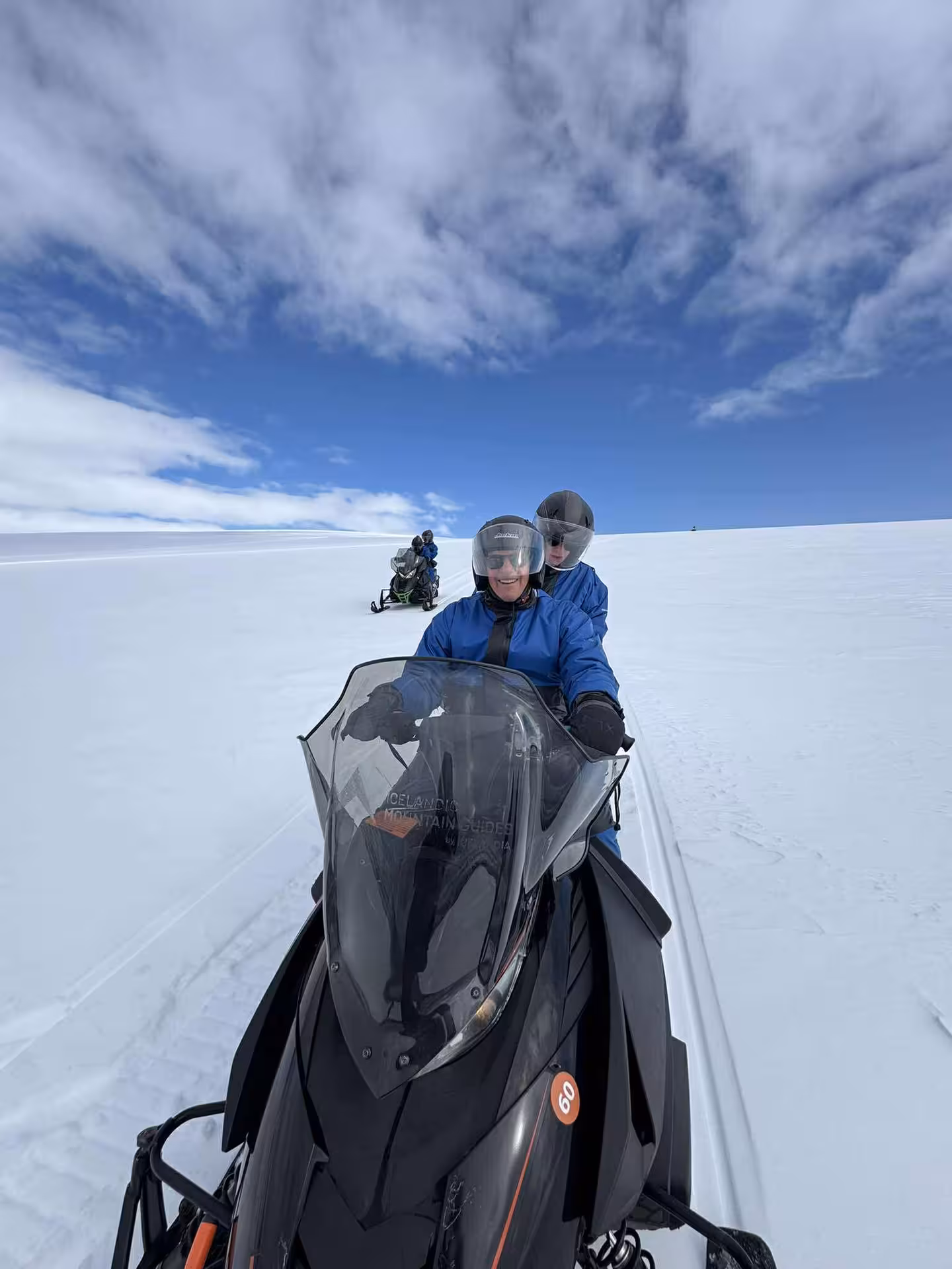 Two riders in blue suits snowmobiling on Langjokull glacier under a blue sky in Iceland