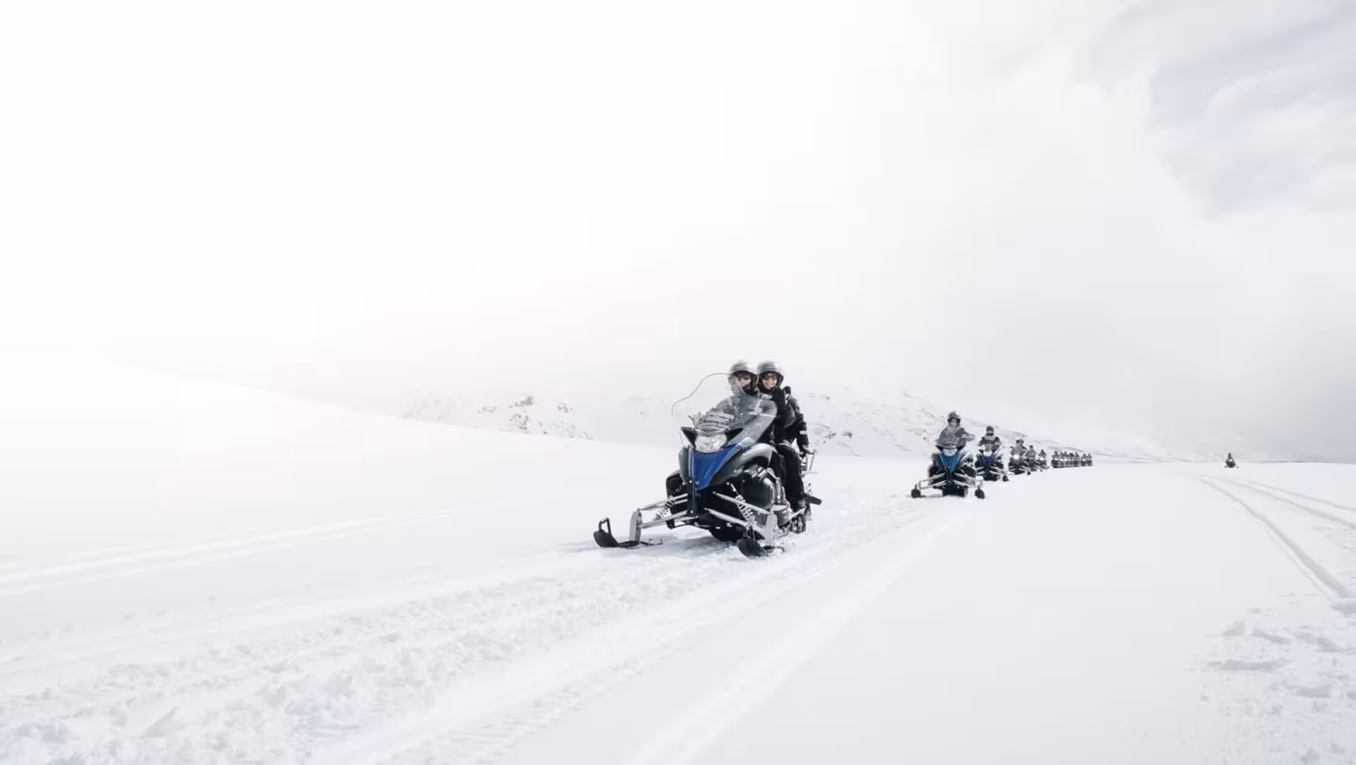 Group of snowmobilers riding in a line across a vast snowy glacier in Iceland