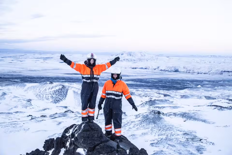 Two guides in orange safety suits and helmets standing on snowy Eyjafjallajokull volcano summit