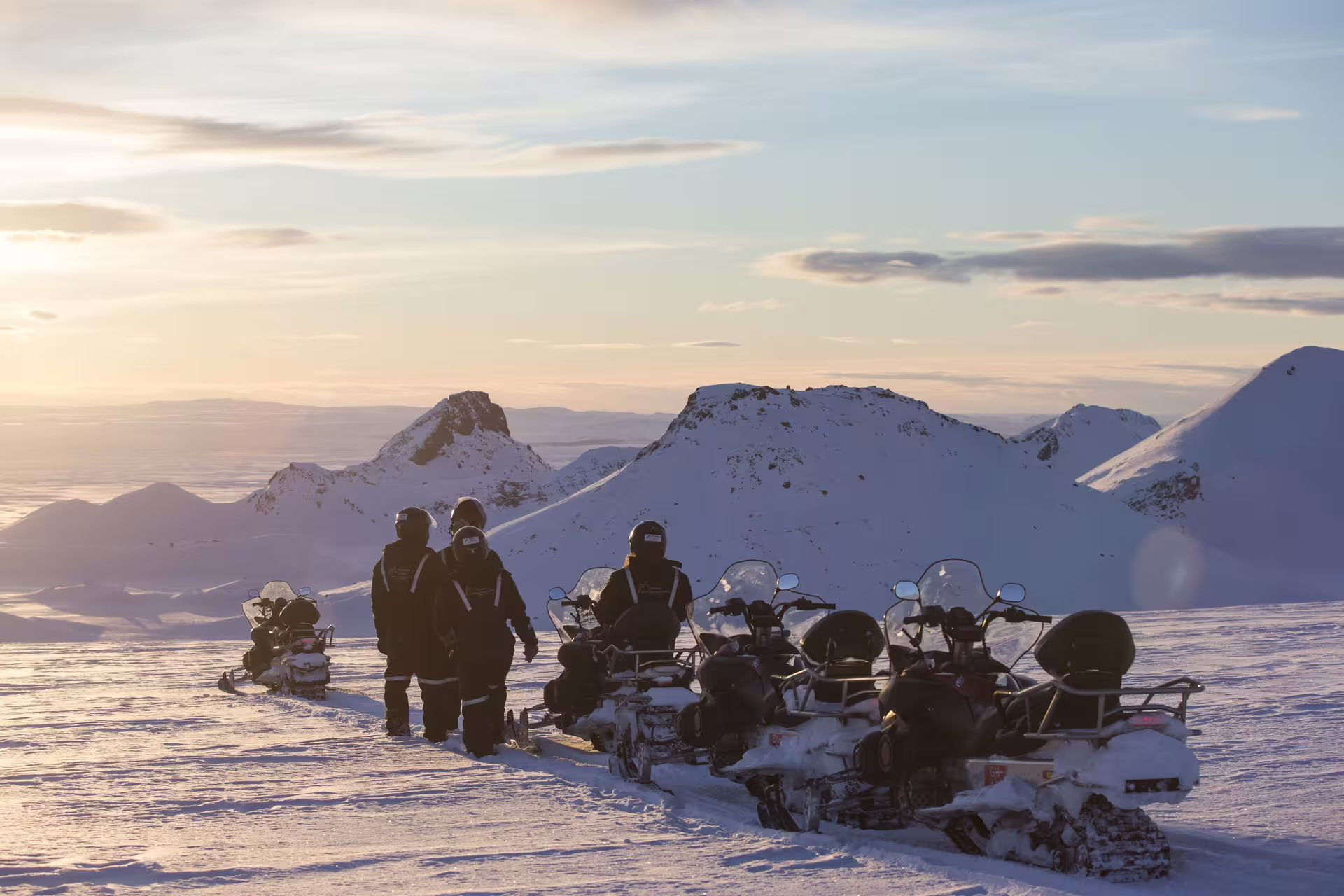 Group of snowmobilers pausing on a snowy glacier with snow-capped mountains and golden sunset in Iceland