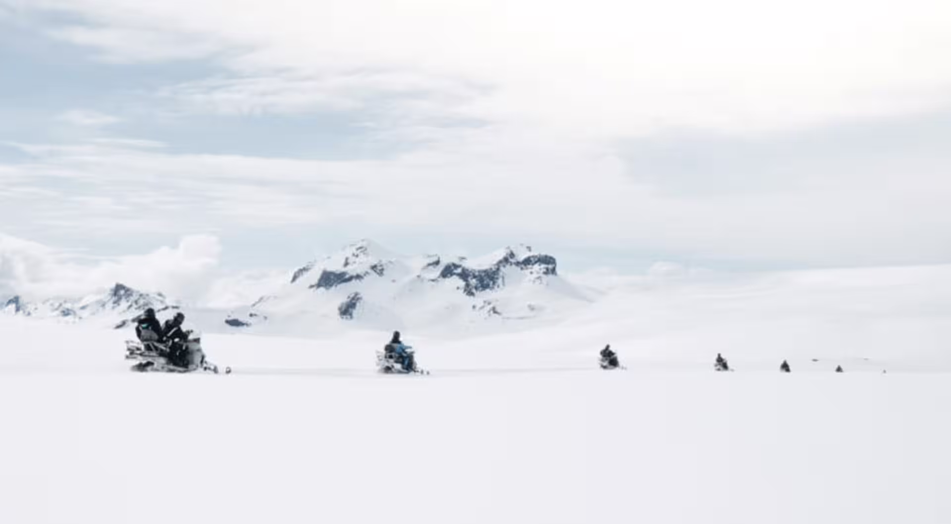 Group of snowmobilers crossing a vast snowy glacier with snow-capped mountains in Iceland