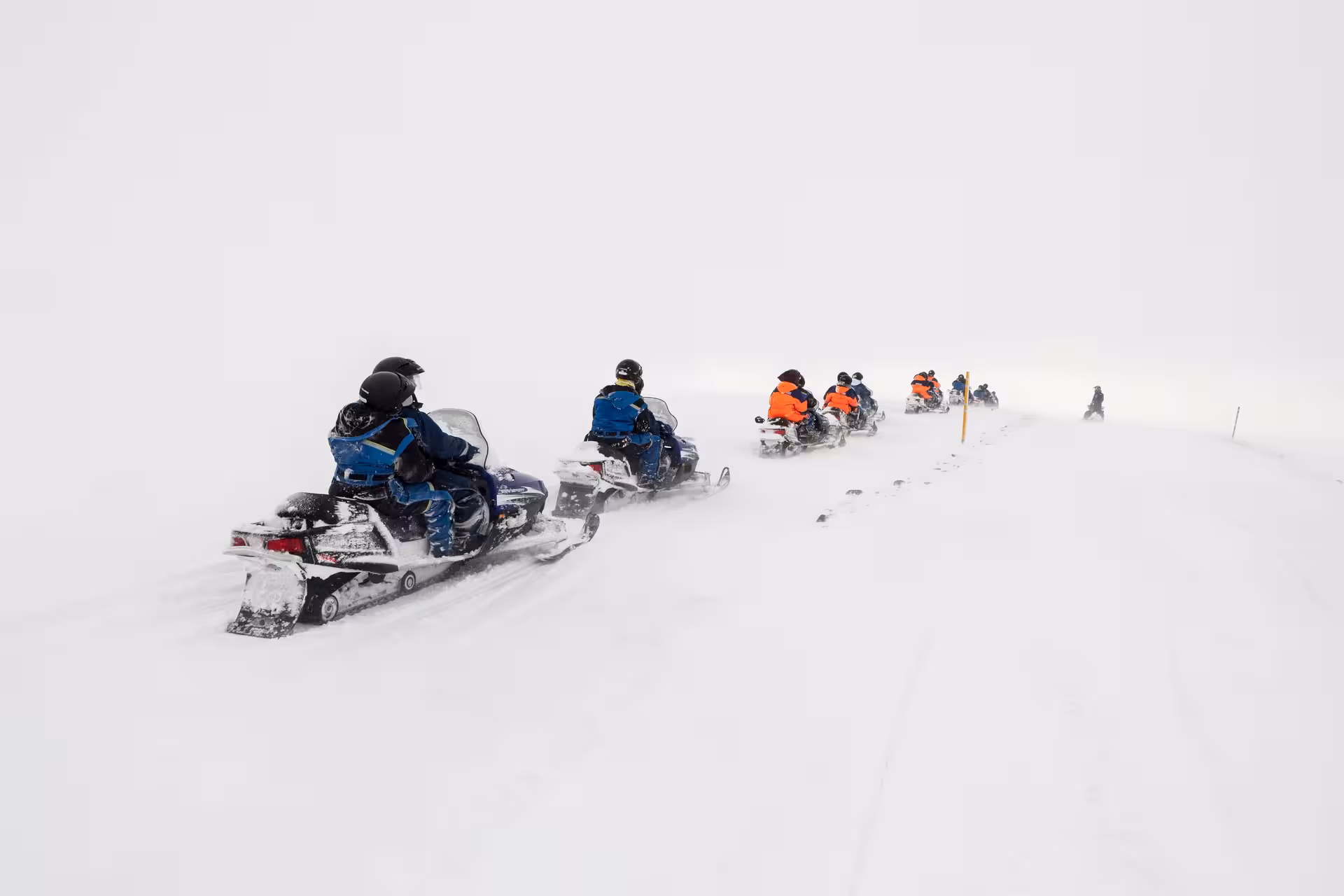 Group of snowmobilers riding in a line across a vast snowy glacier on the Silver Circle private day tour in Borgarfjordur Iceland