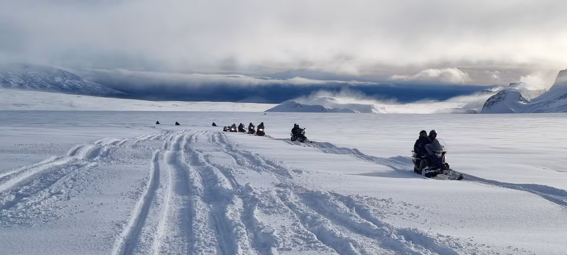 Convoy of snowmobiles leaving fresh tracks on an Iceland glacier during an adventurous Golden Circle snowmobile tour