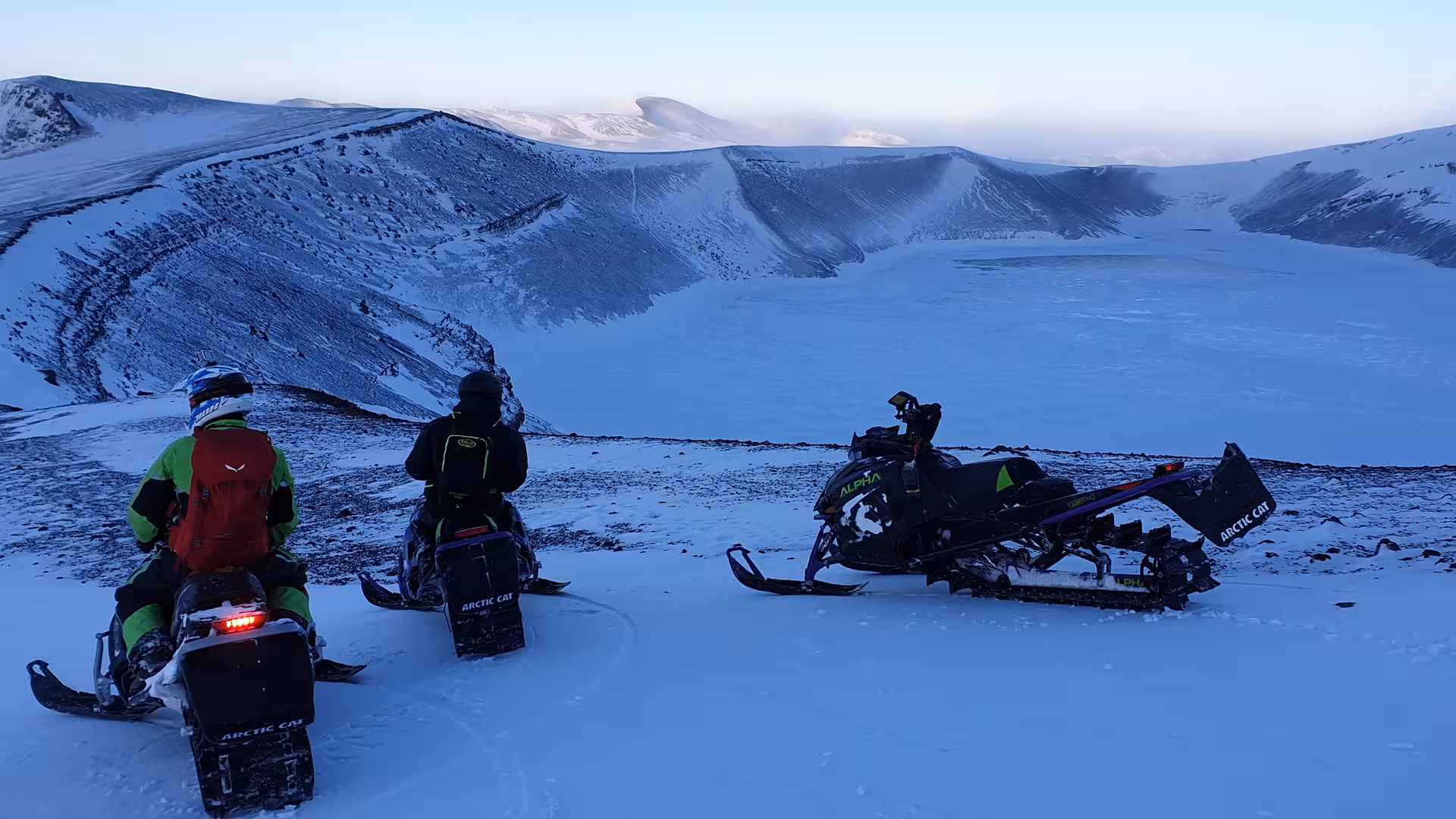 Two snowmobilers on Arctic Cat sleds overlooking a frozen volcanic crater in Landmannalaugar Highlands
