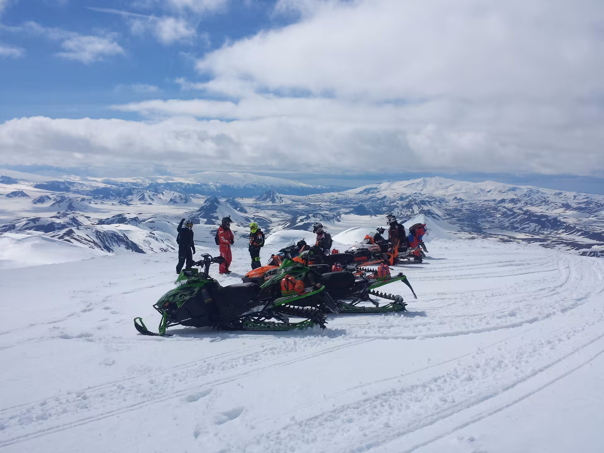 Group of snowmobilers resting with Arctic Cat snowmobiles on snowy Landmannalaugar Highland plateau
