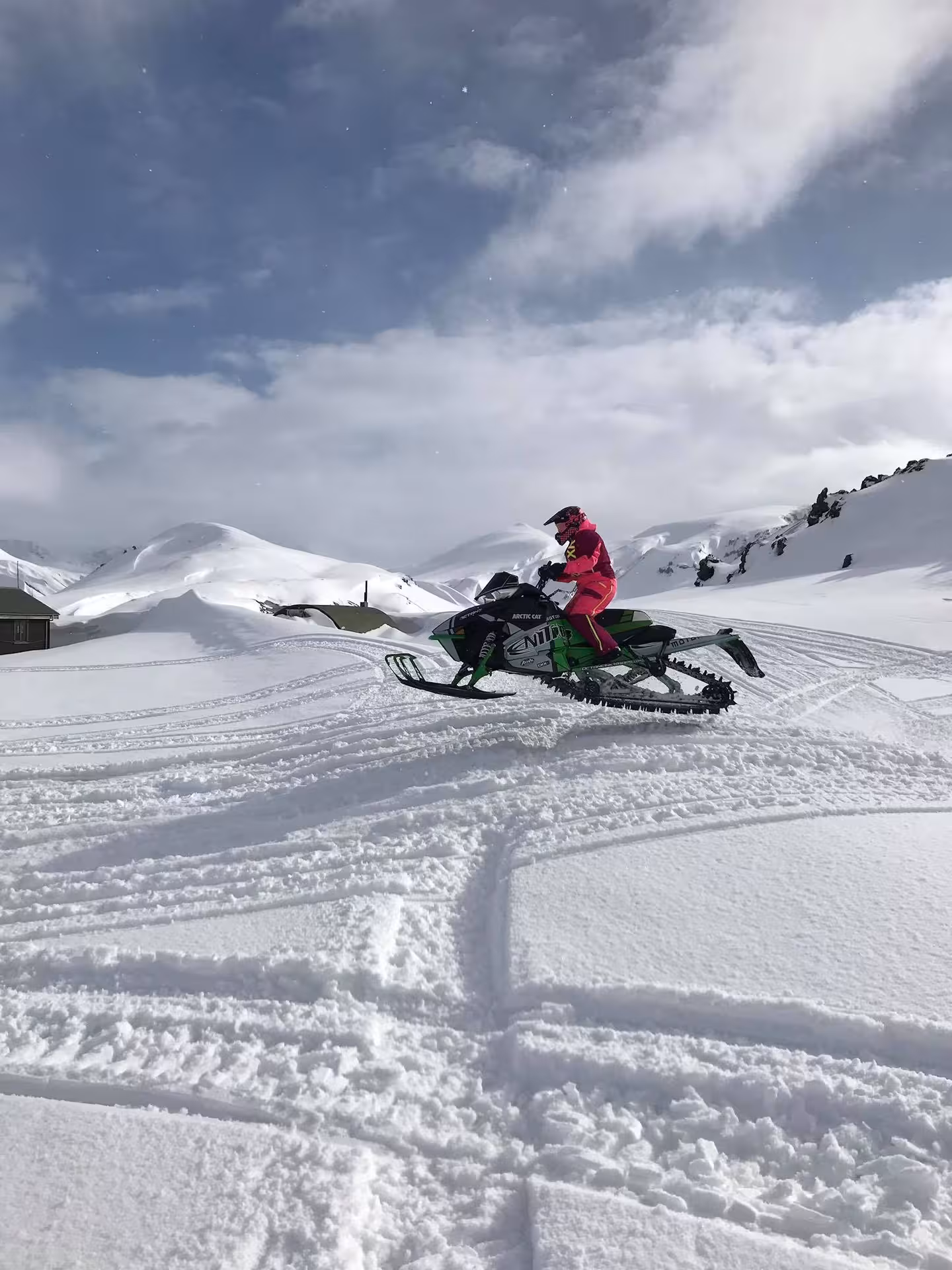 Rider in pink suit on green Arctic Cat snowmobile crossing snowy Landmannalaugar highlands terrain