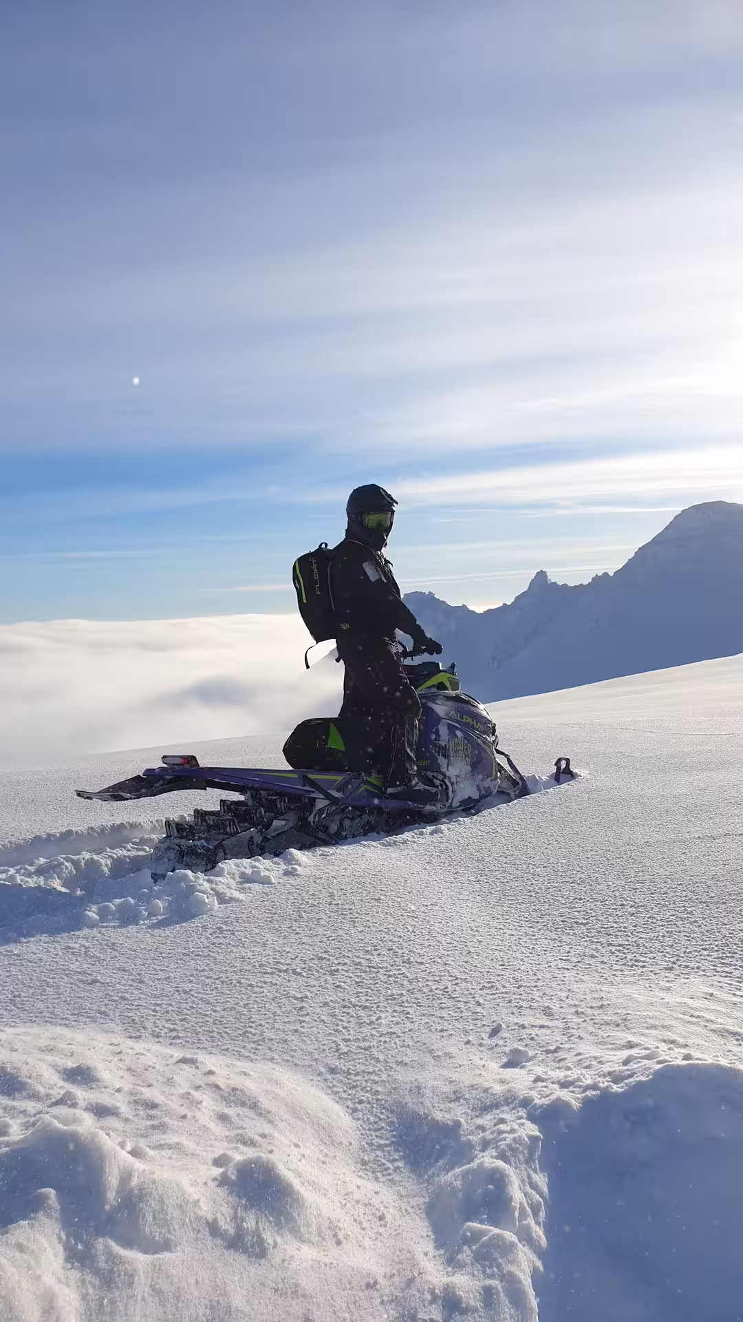 Snowmobiler riding through deep powder snow in highland mountains on a sunny winter day