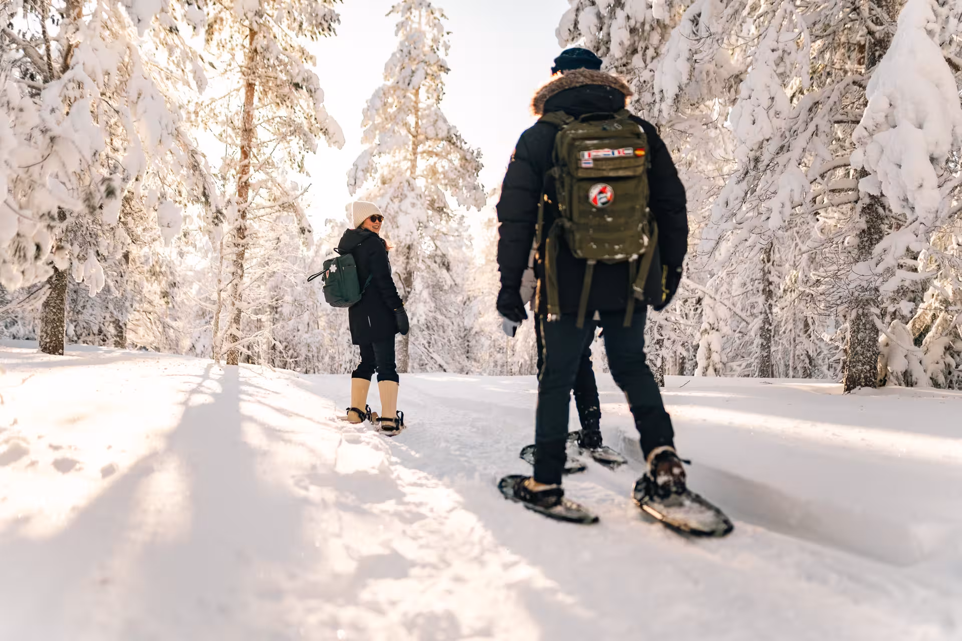 Adventurers snowshoeing through Rovaniemi's sunlit Arctic wilderness, surrounded by snow-covered trees and pristine trails.