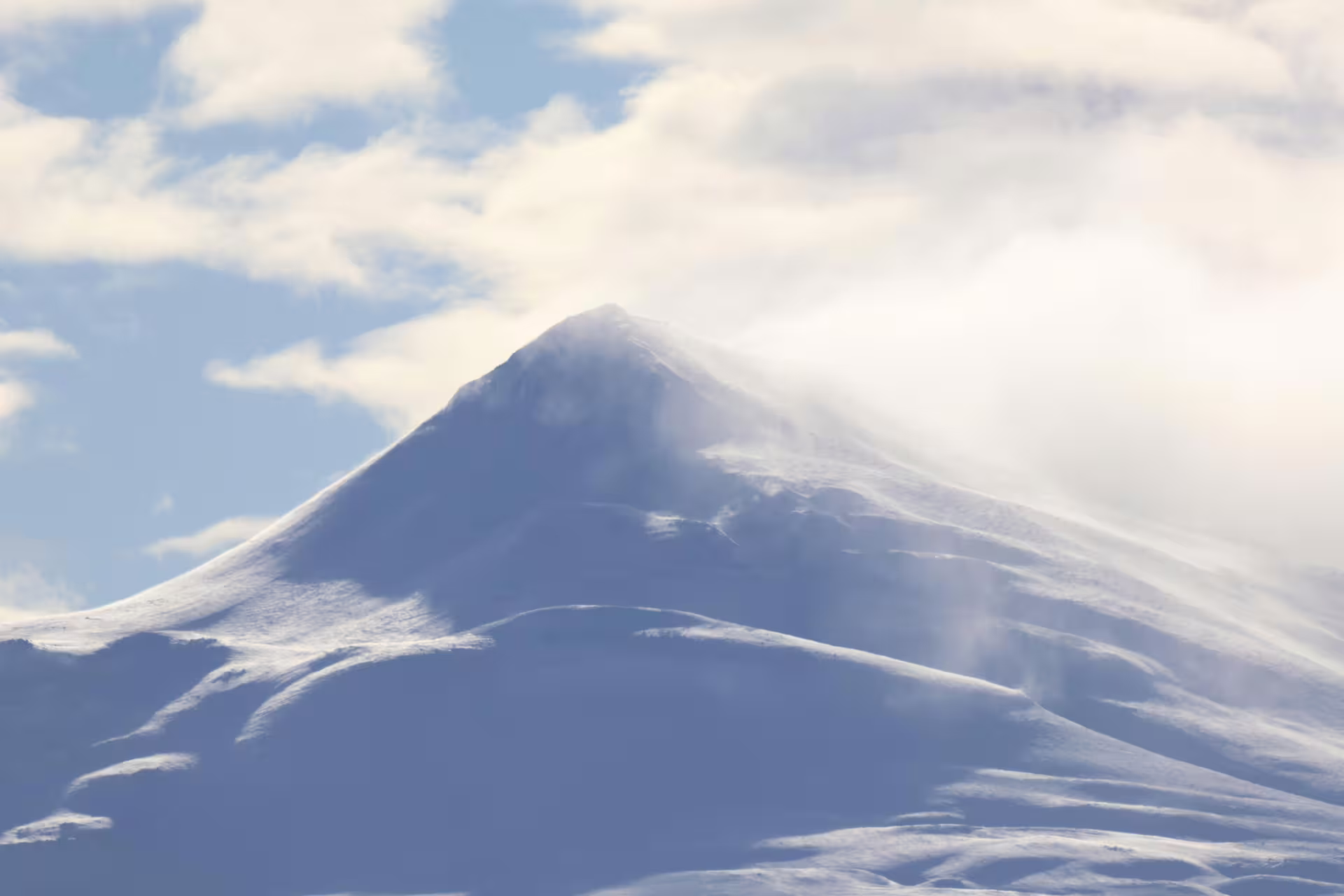 Snow-covered mountain peak with wind-blown snow and clouds near Akureyri, Iceland