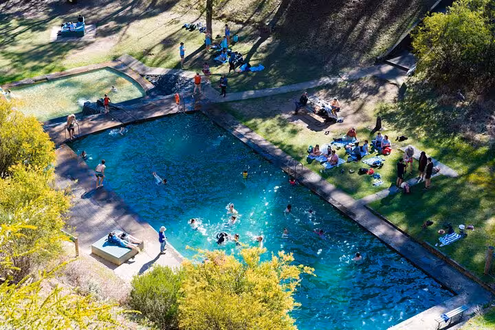 Aerial view of people enjoying a pool surrounded by lush greenery, part of the Snowy Mountains NSW tour experience.
