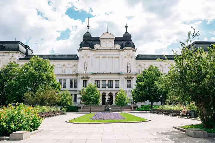 White neoclassical building with ornate domes, garden courtyard, and statue in Sofia, Bulgaria
