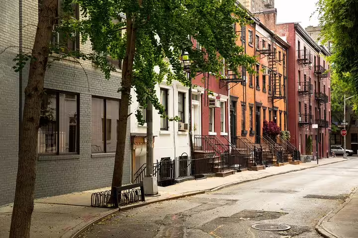Tree-lined SoHo NYC street with colorful brick townhouses, iron staircases, and fire escapes
