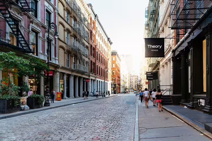 Cobblestone street in SoHo NYC lined with historic cast-iron buildings and pedestrians walking past boutique shops