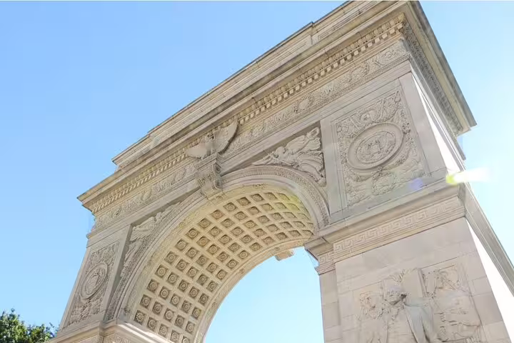 Ornate marble arch with detailed carvings and coffered ceiling against blue sky in NYC