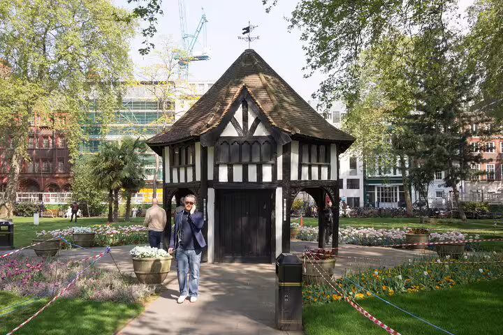 Tudor-style garden pavilion in Soho square park with flower beds and urban buildings in background