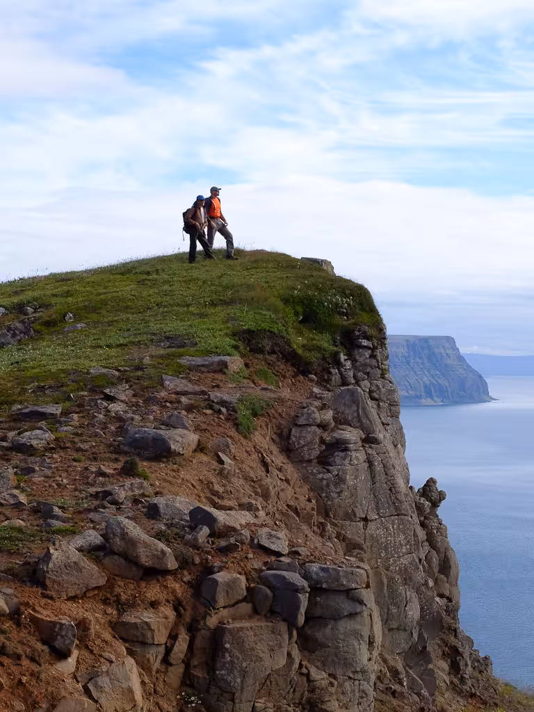 Hikers on a coastal cliff summit during a Solar Eclipse Hike, scenic viewpoint trek with ocean panorama
