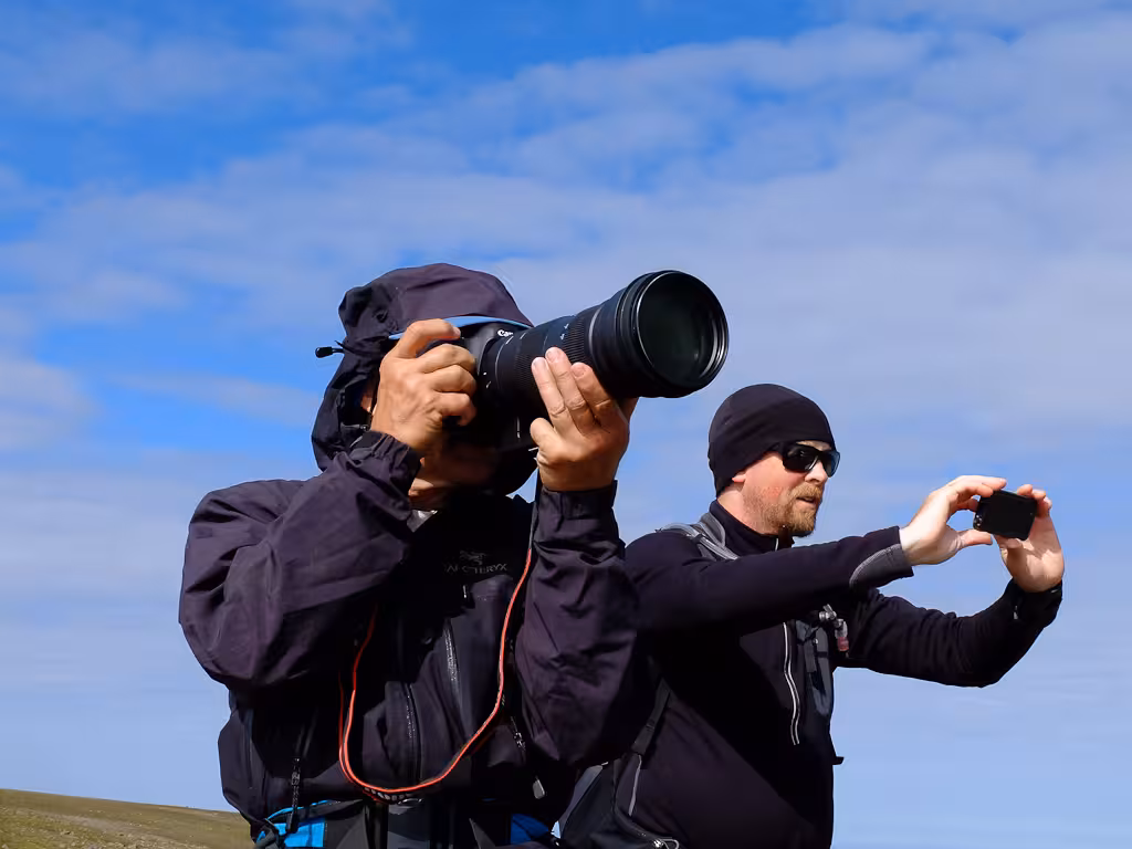 Photographers on ridge capturing the solar eclipse on guided hike, using telephoto lens and phone under blue sky