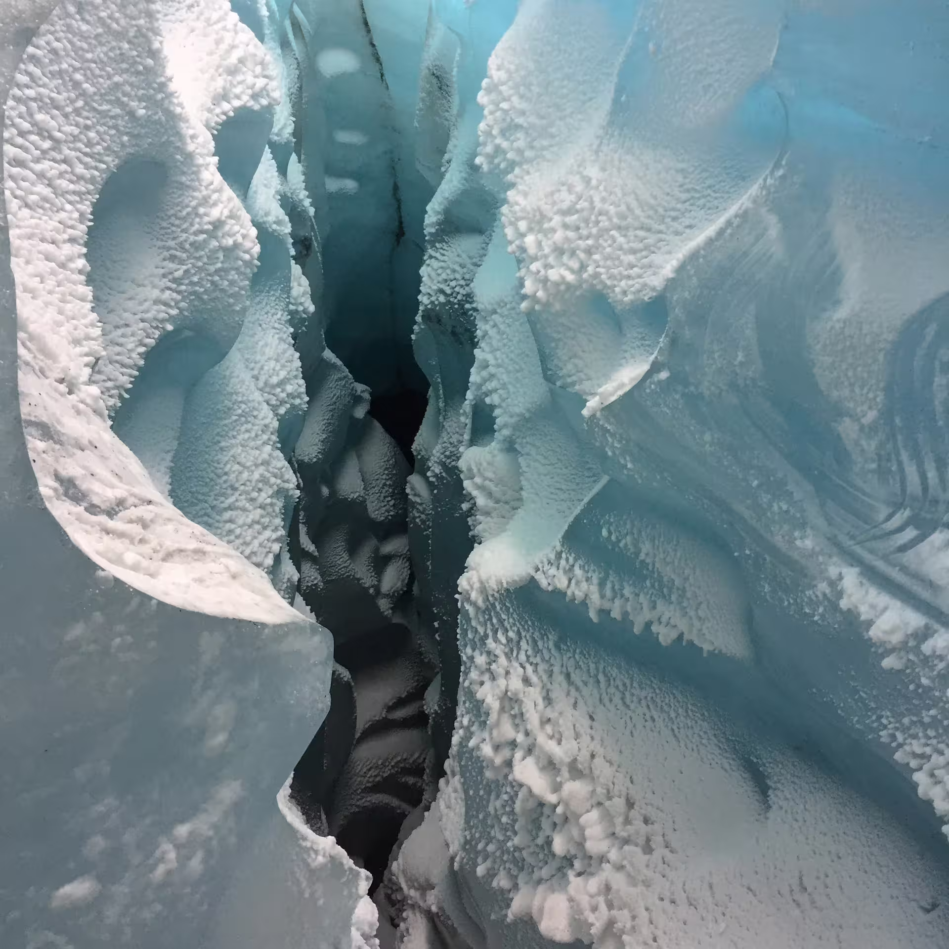 Deep glacial crevasse with layered blue ice and snow crystals at Solheimajokull glacier