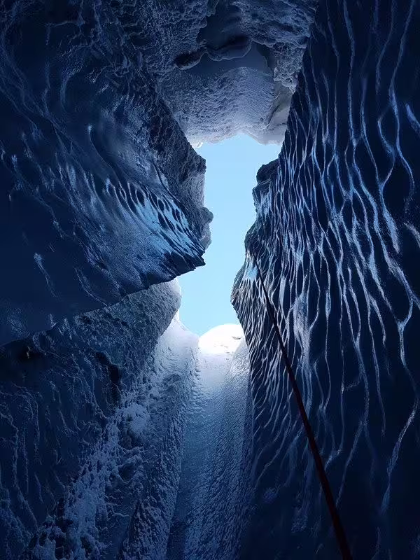 Deep glacial crevasse with blue ice walls and narrow opening to sky at Solheimajokull glacier