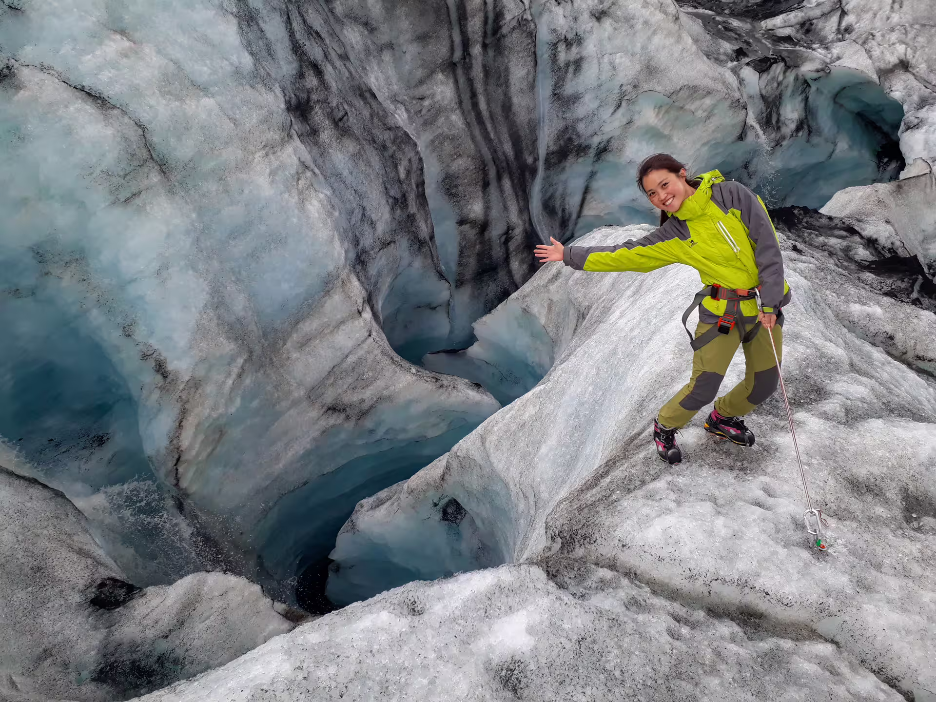 Female hiker in green jacket with ice axe posing on Solheimajokull glacier crevasse, Iceland