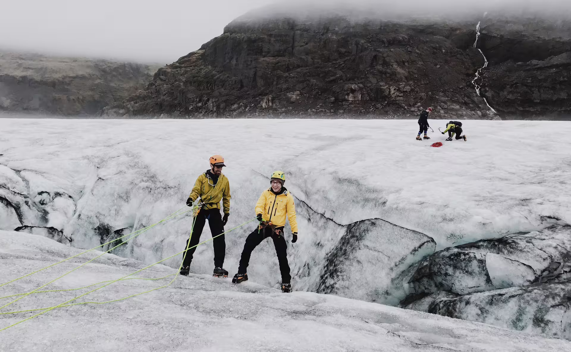 Two climbers in yellow jackets and helmets ice climbing on Solheimajokull glacier with ropes and crampons