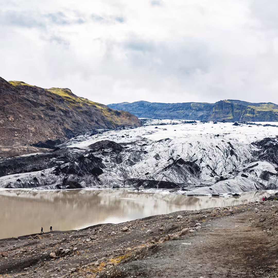 Hikers exploring Solheimajokull glacier with glacial lagoon and volcanic mountains on private Iceland tour
