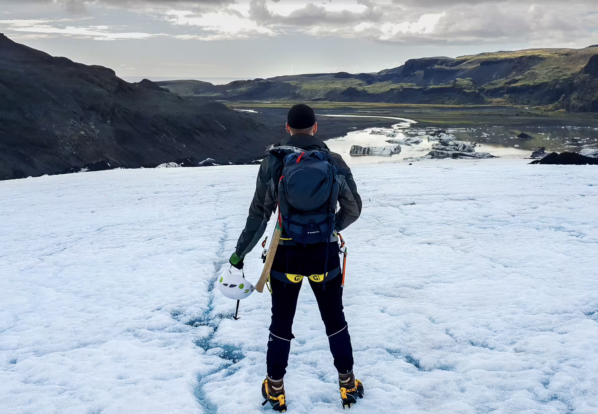 Hiker with crampons and ice axe standing on Solheimajokull glacier overlooking glacial lagoon in Iceland