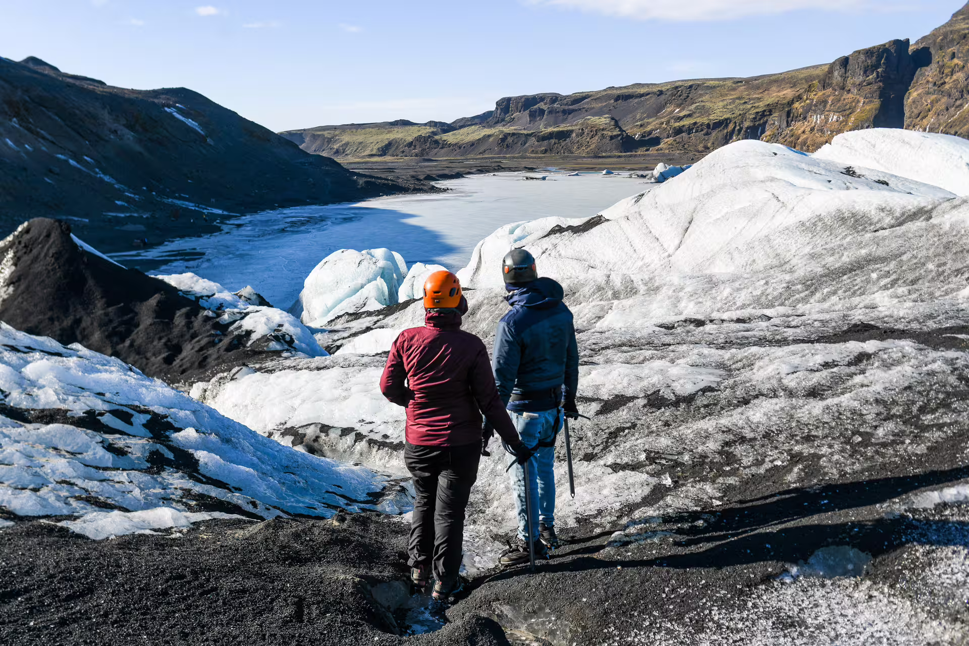 Two hikers with helmets and ice axes explore the rugged black and white terrain of Sólheimajökull Glacier Iceland