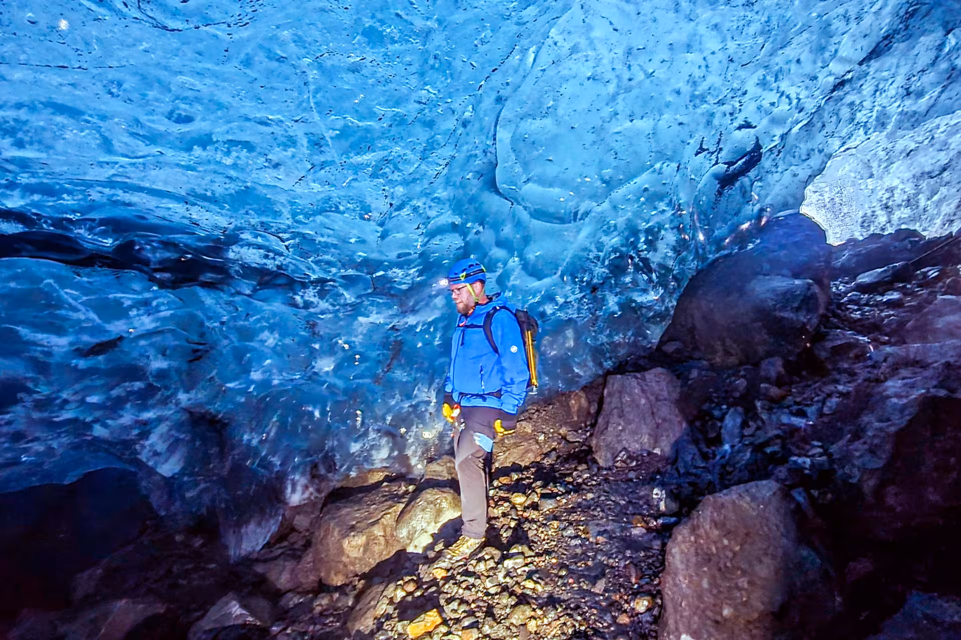 Explorer in blue jacket and helmet standing inside glowing blue Solheimajokull glacier ice cave