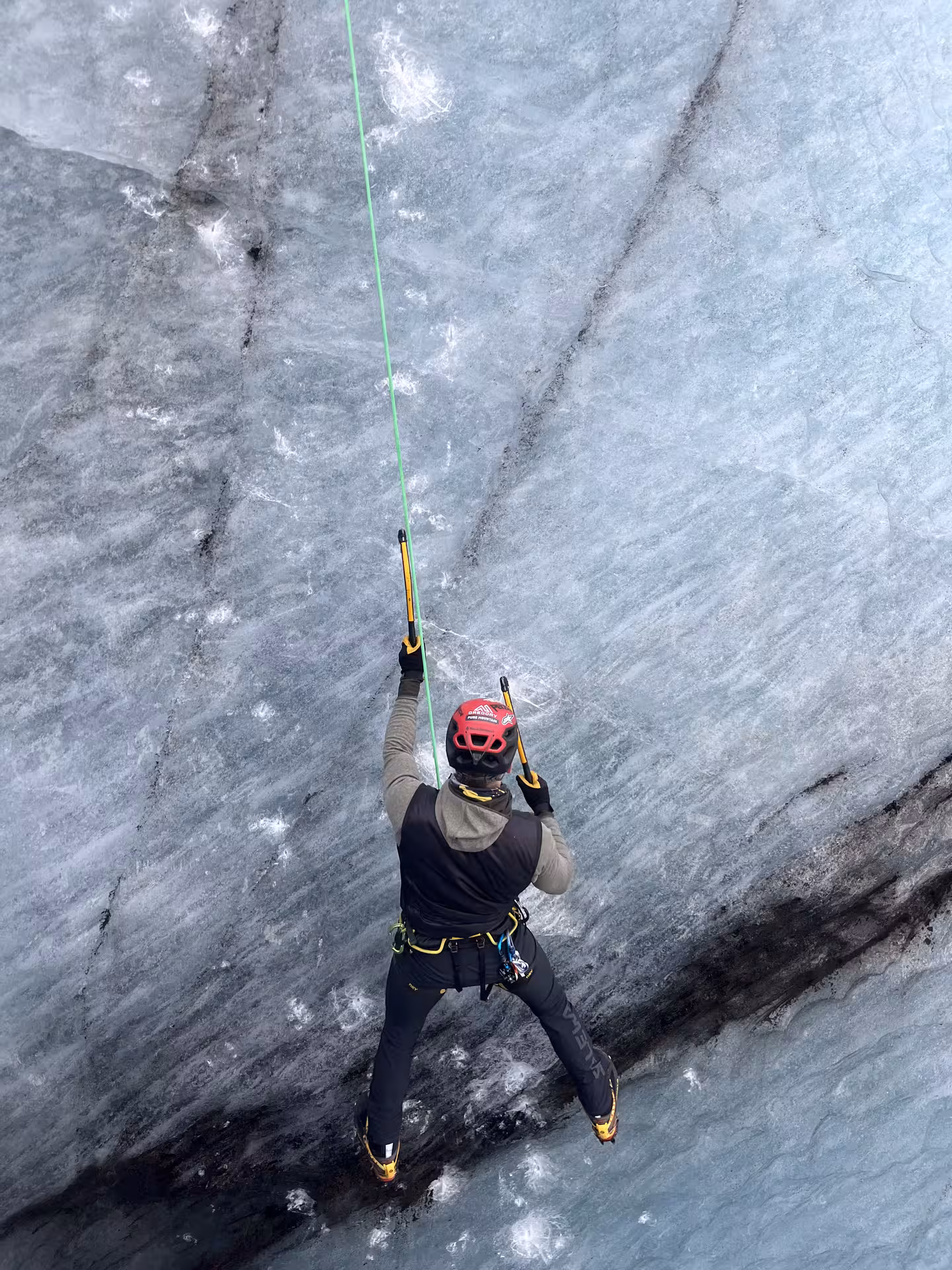 Close-up of climber on Sólheimajökull glacier ice wall, using ice axes on guided ice climbing tour