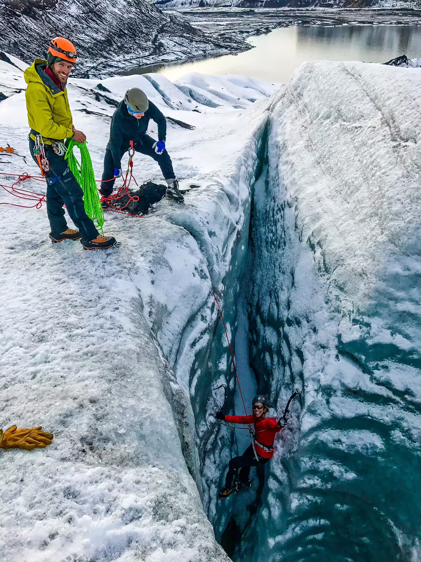 Climber ascending glacial crevasse with ice axes while two guides manage ropes on Solheimajokull glacier