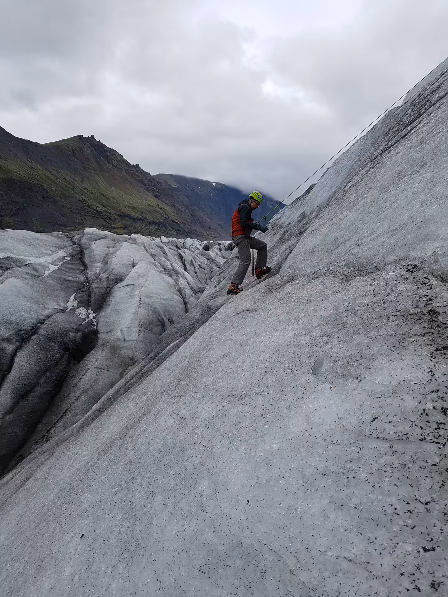 Climber with helmet and crampons ascending steep ice wall on Solheimajokull glacier with rope belay