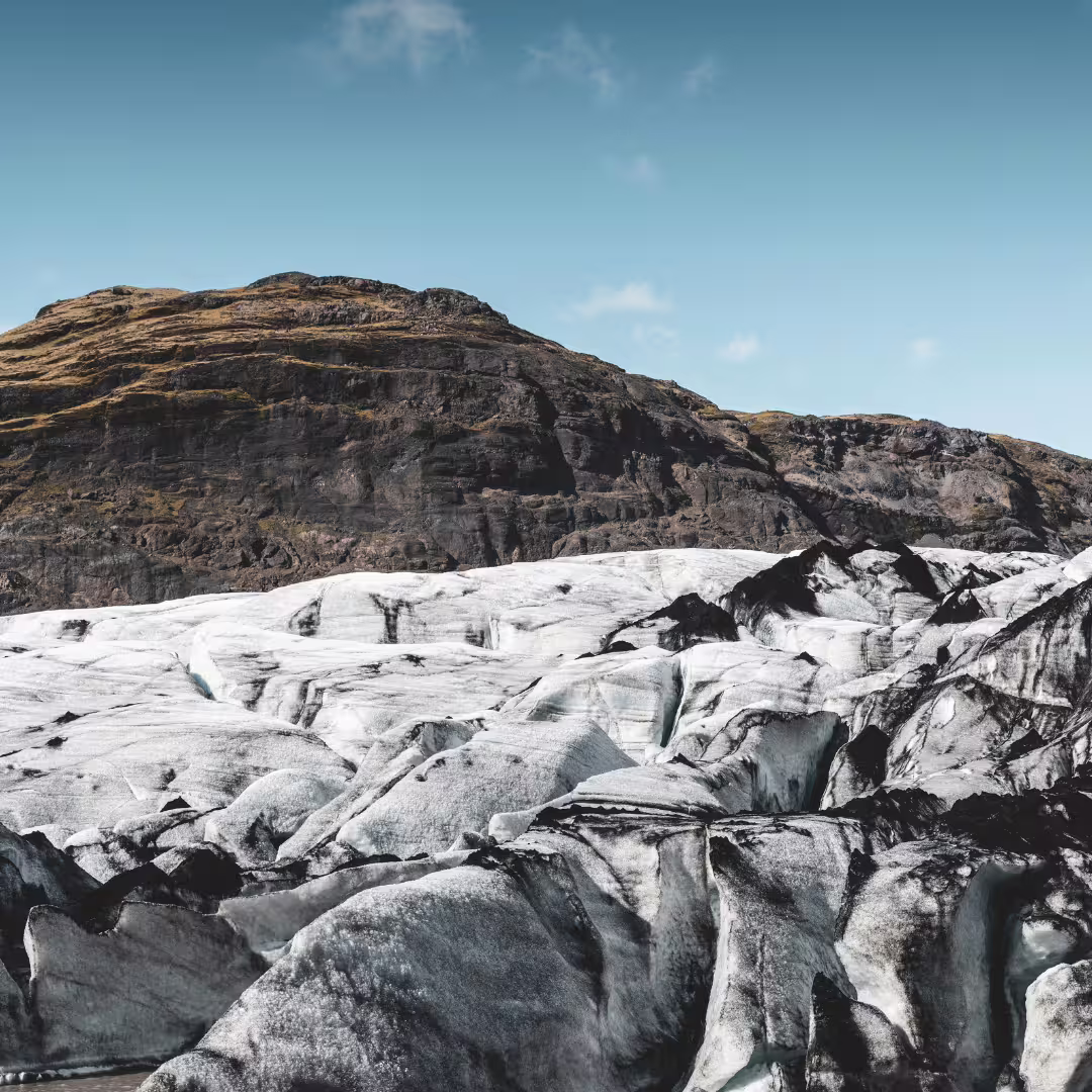 Dramatic Solheimajokull glacier ice surface with jagged formations and volcanic mountain backdrop in Iceland