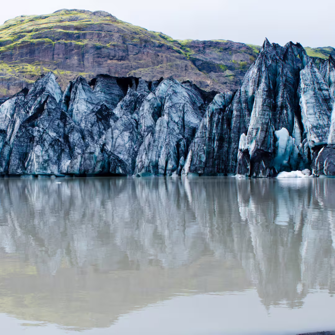 Dramatic jagged ice formations at Solheimajokull Glacier reflecting in glacial lagoon on a private Iceland hike tour.