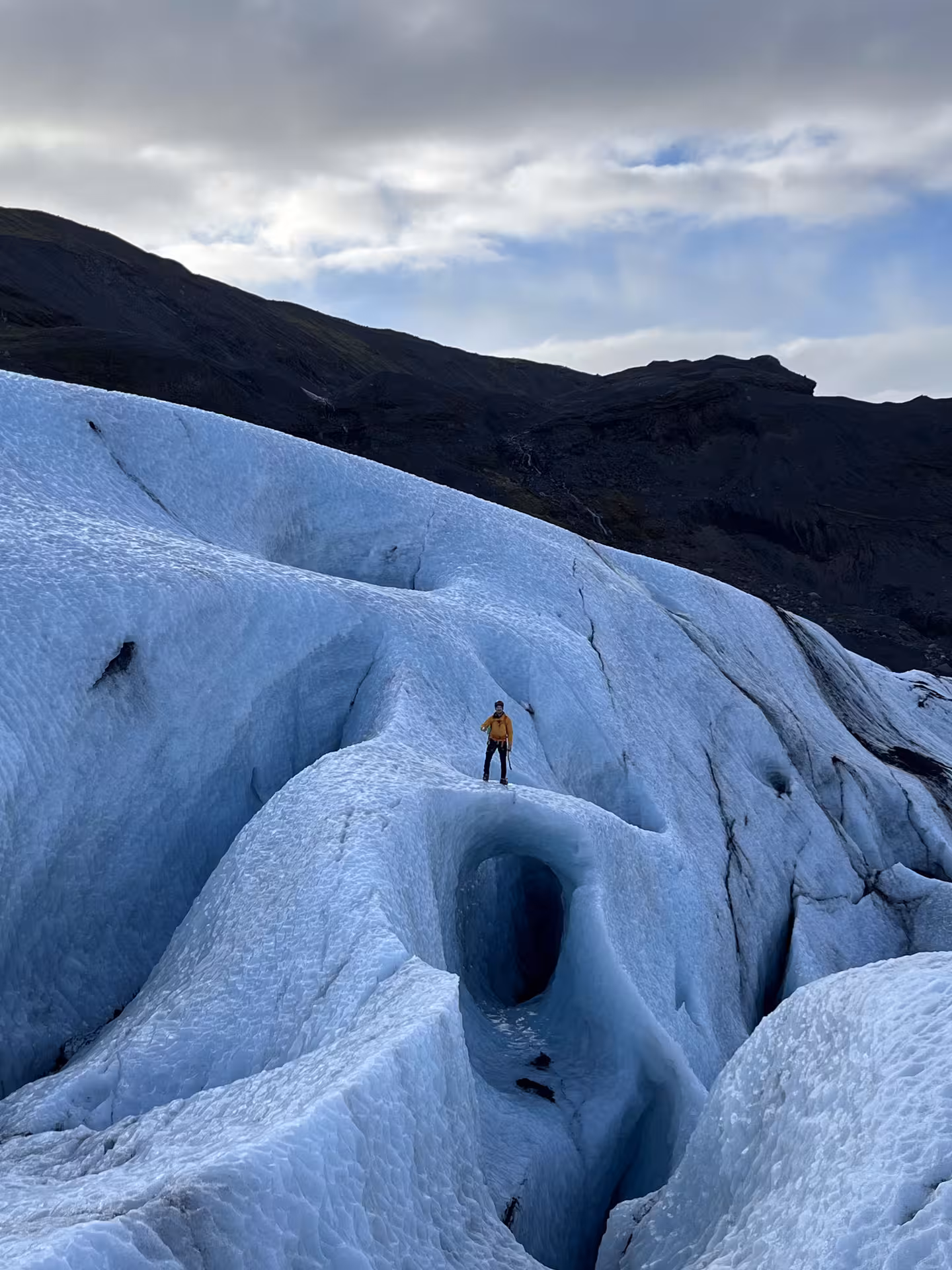 Hiker stands above a deep glacier moulin on Sólheimajökull, a highlight of Iceland glacier hike and ice climbing