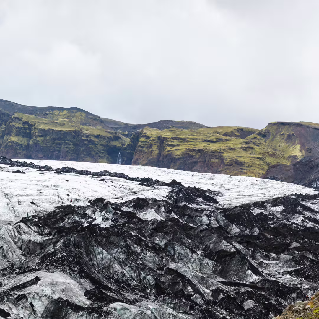 Vast Solheimajokull Glacier covered in black volcanic ash with hikers exploring on a private Iceland glacier tour.
