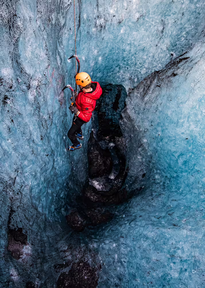 Climber scaling stunning blue ice walls with ice axes on a private Solheimajokull Glacier ice climbing adventure